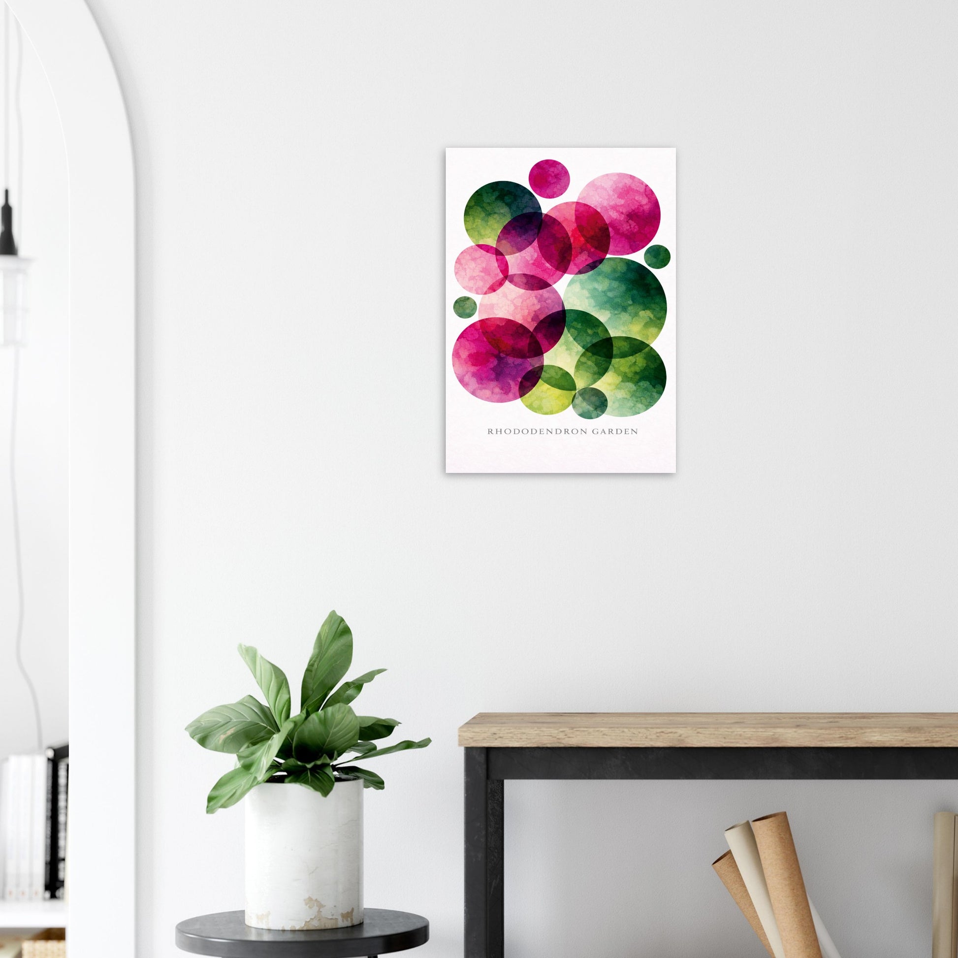 A framed wall art print featuring overlapping watercolor circles in pink, magenta, green, and teal on a white background, displayed above a console table with a potted plant in a modern interior setting.