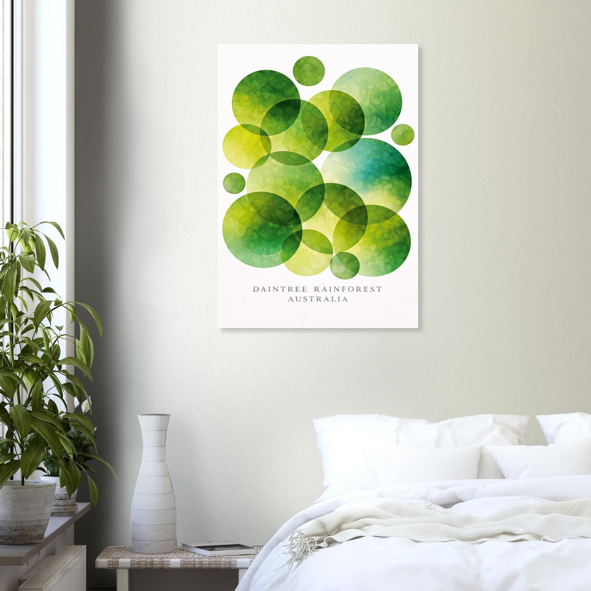A vertical wall art print featuring overlapping green watercolor circles on a white background, with the text 'DAINTREE RAINFOREST AUSTRALIA' near the bottom. The print is displayed in a bedroom setting above a bed with white bedding, next to a potted plant and a vase.