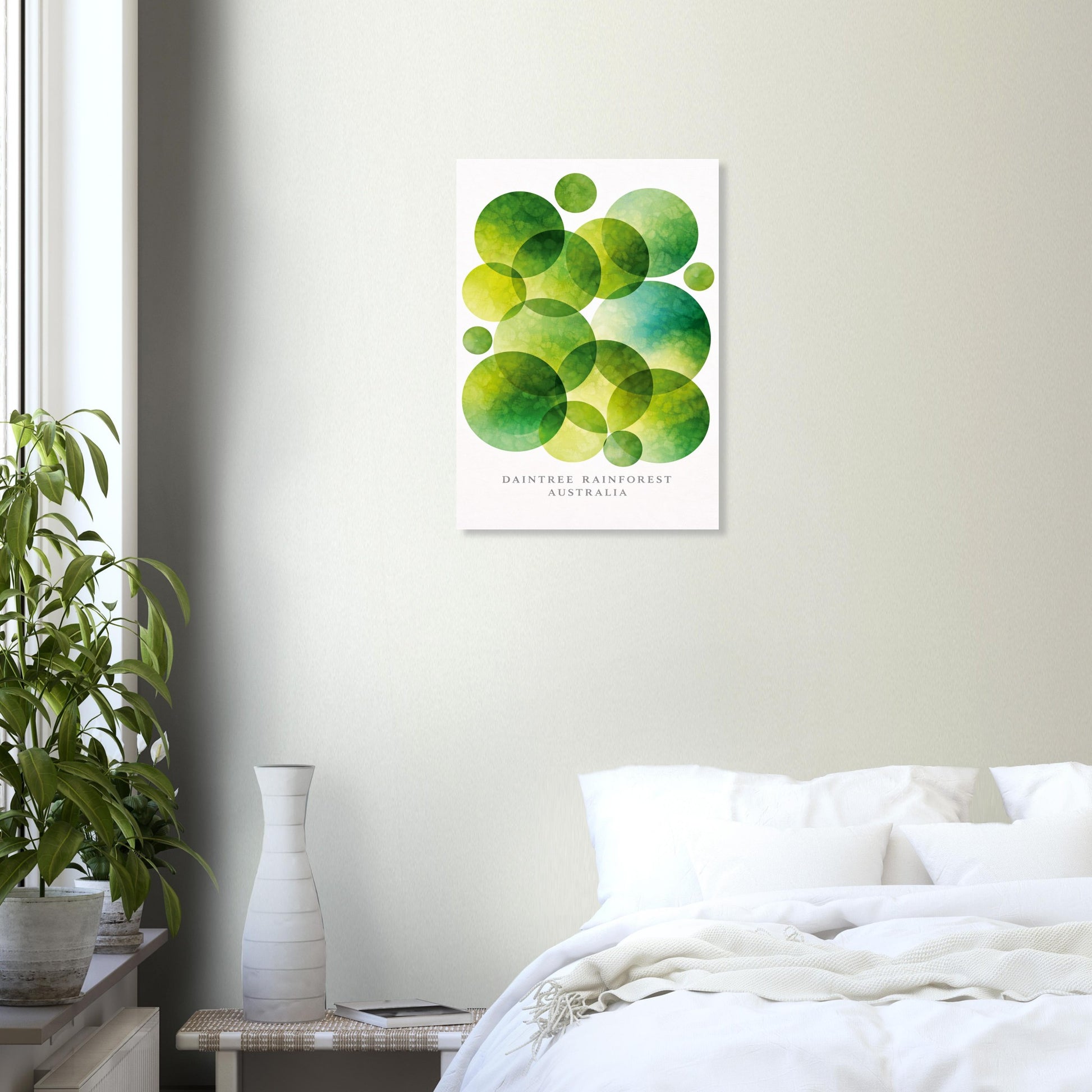 A vertical wall art print featuring overlapping green watercolor circles on a white background displayed above a bed in a softly lit bedroom with a plant and vase.