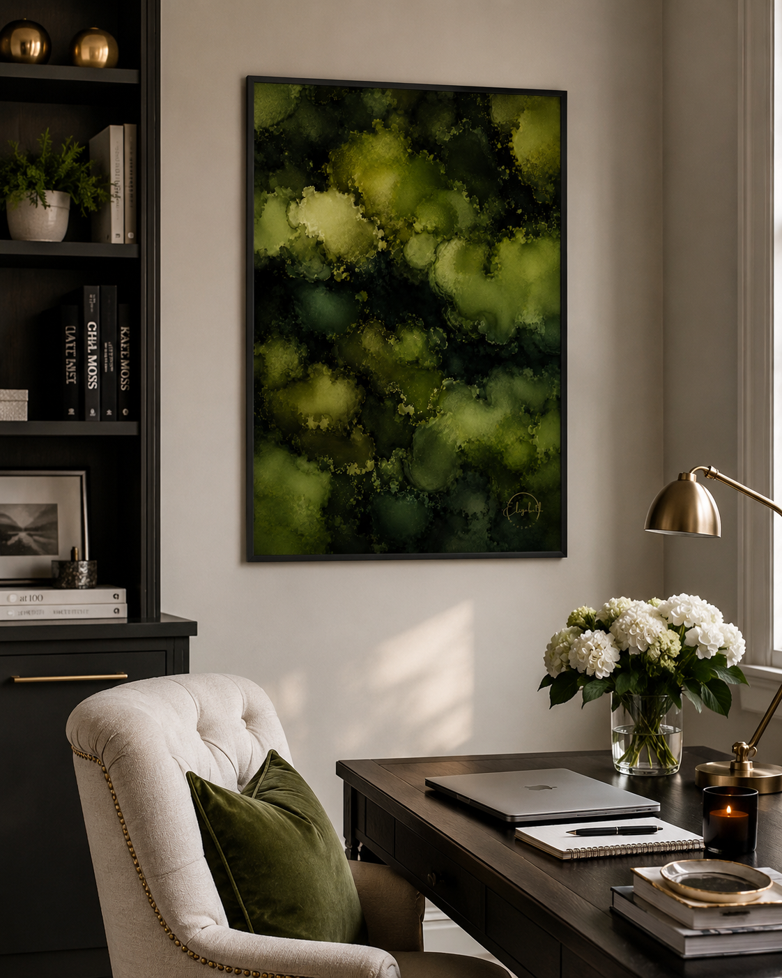 A framed abstract art print featuring shades of green and black, displayed on a neutral wall in a styled home office setting with a desk, chair, and lamp.