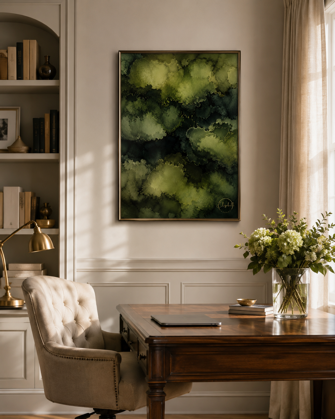 A framed abstract art print featuring shades of olive green and black, displayed on a beige wall in a beautifully styled home office with a wooden desk, tufted armchair, and a vase of white flowers.