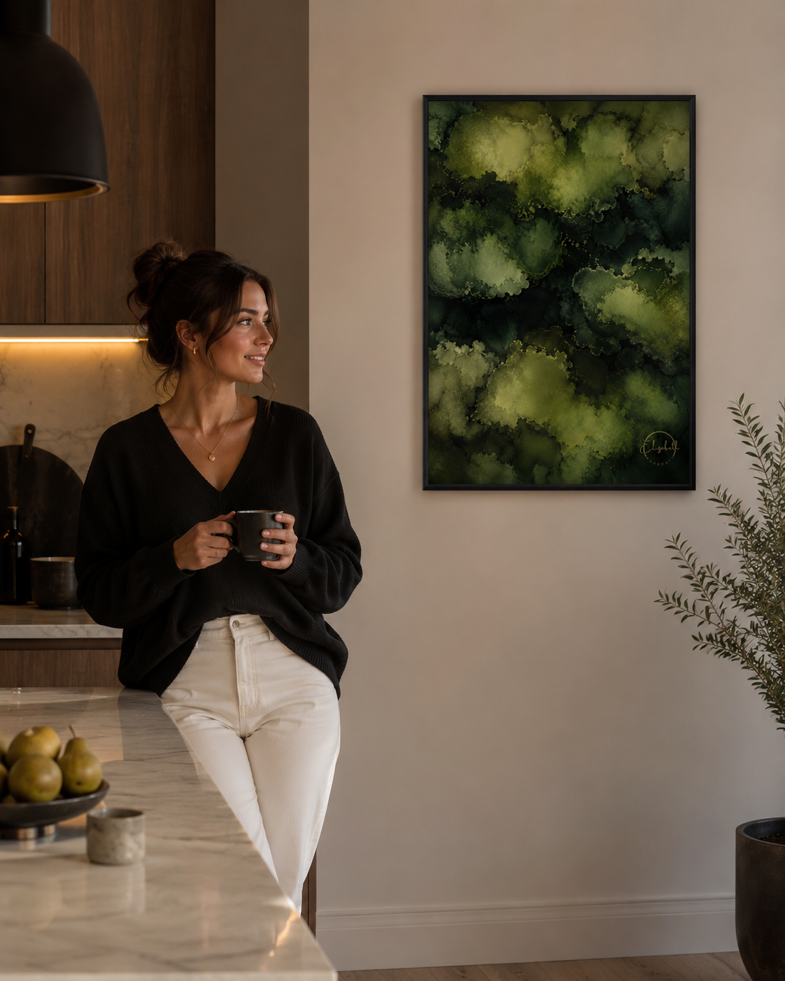 A woman in a black top and white pants stands in a modern kitchen setting, holding a black mug. On the wall above her is a framed abstract art print featuring textured green and dark green brushstrokes.