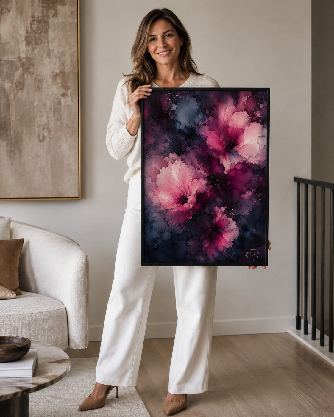 A woman in a white outfit holds up a framed abstract floral painting featuring pink and purple flowers on a dark background, set in a modern living room interior.