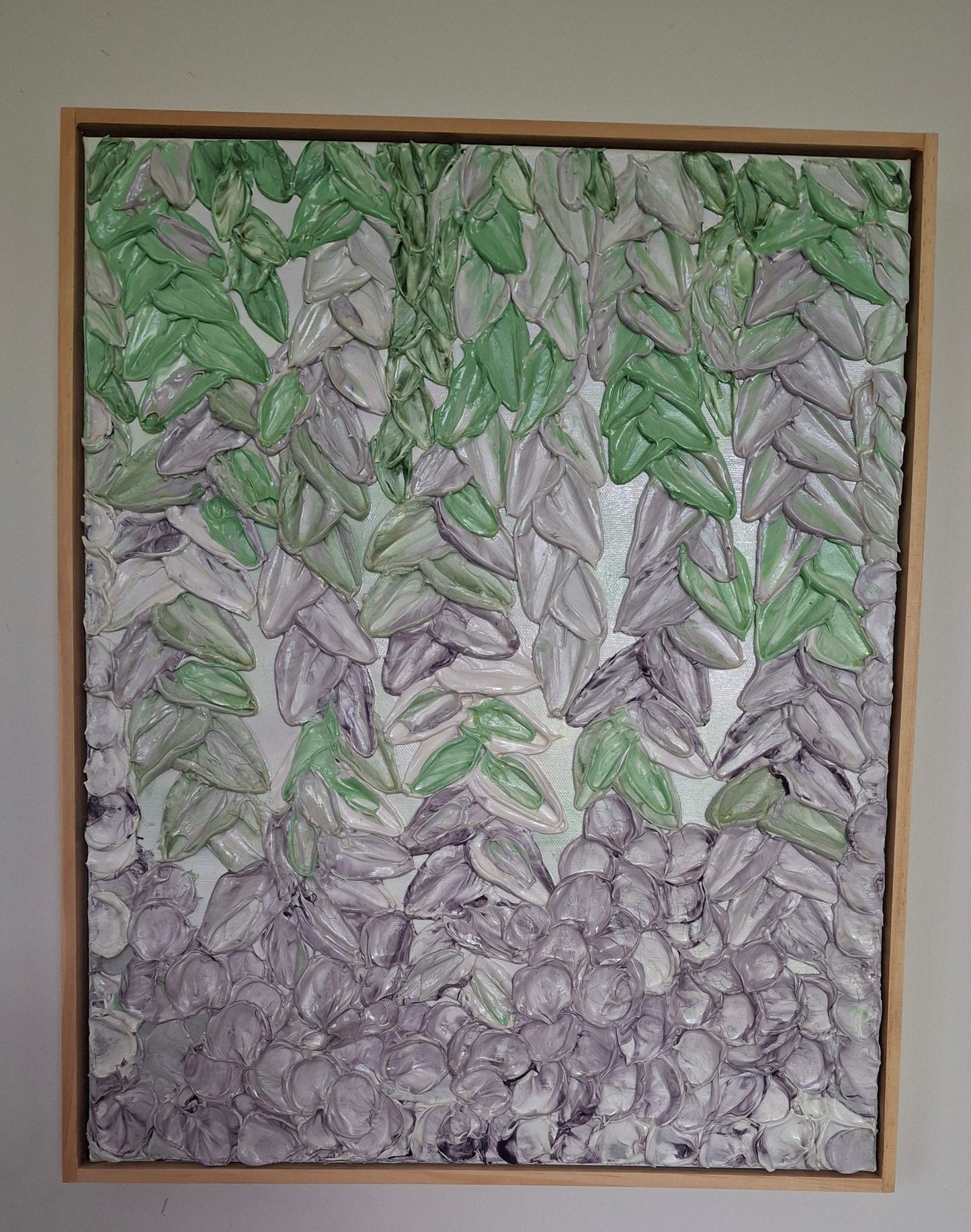 A framed abstract painting featuring textured green and gray leaf-like forms on a white background, hung on a plain light gray wall.