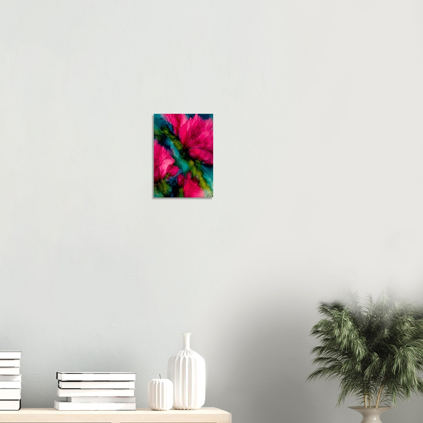 A small vertical wall art print featuring a vivid abstract floral design in hot pink, teal, and green, displayed on a light gray wall above a shelf with books, white vases, and a potted plant.