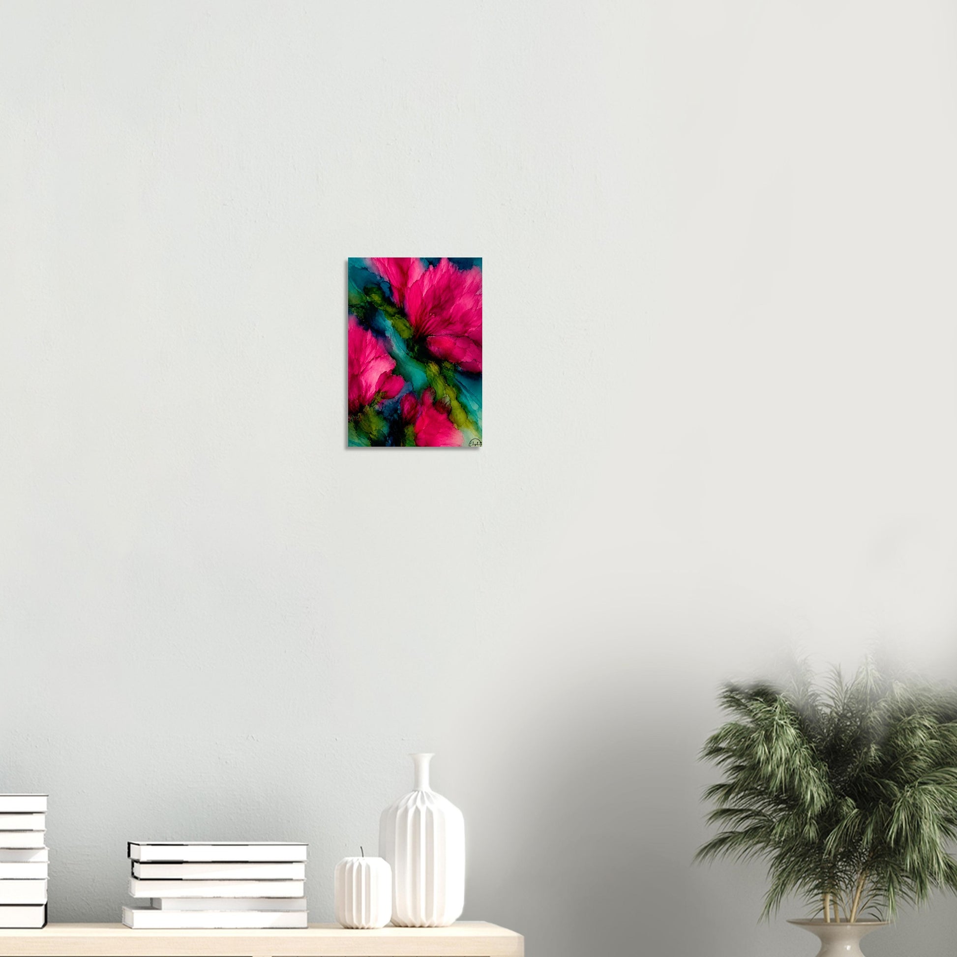 A small vertical wall art print featuring a vivid abstract floral design in hot pink, teal, and green, displayed on a light gray wall above a shelf with books, white vases, and a potted plant.