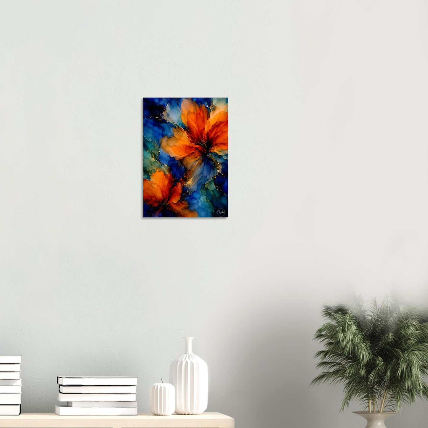 A vertical canvas wall art print featuring an abstract painting of vibrant orange flowers against a deep blue and teal background, displayed on a light gray wall above a console table with books and a plant.