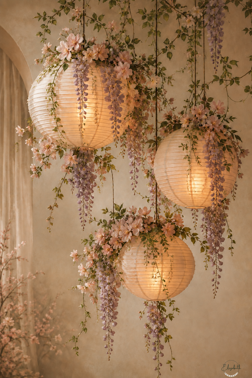 Three glowing round paper lanterns hanging from the ceiling, decorated with cascading wisteria flowers and green vines against a warm beige wall.