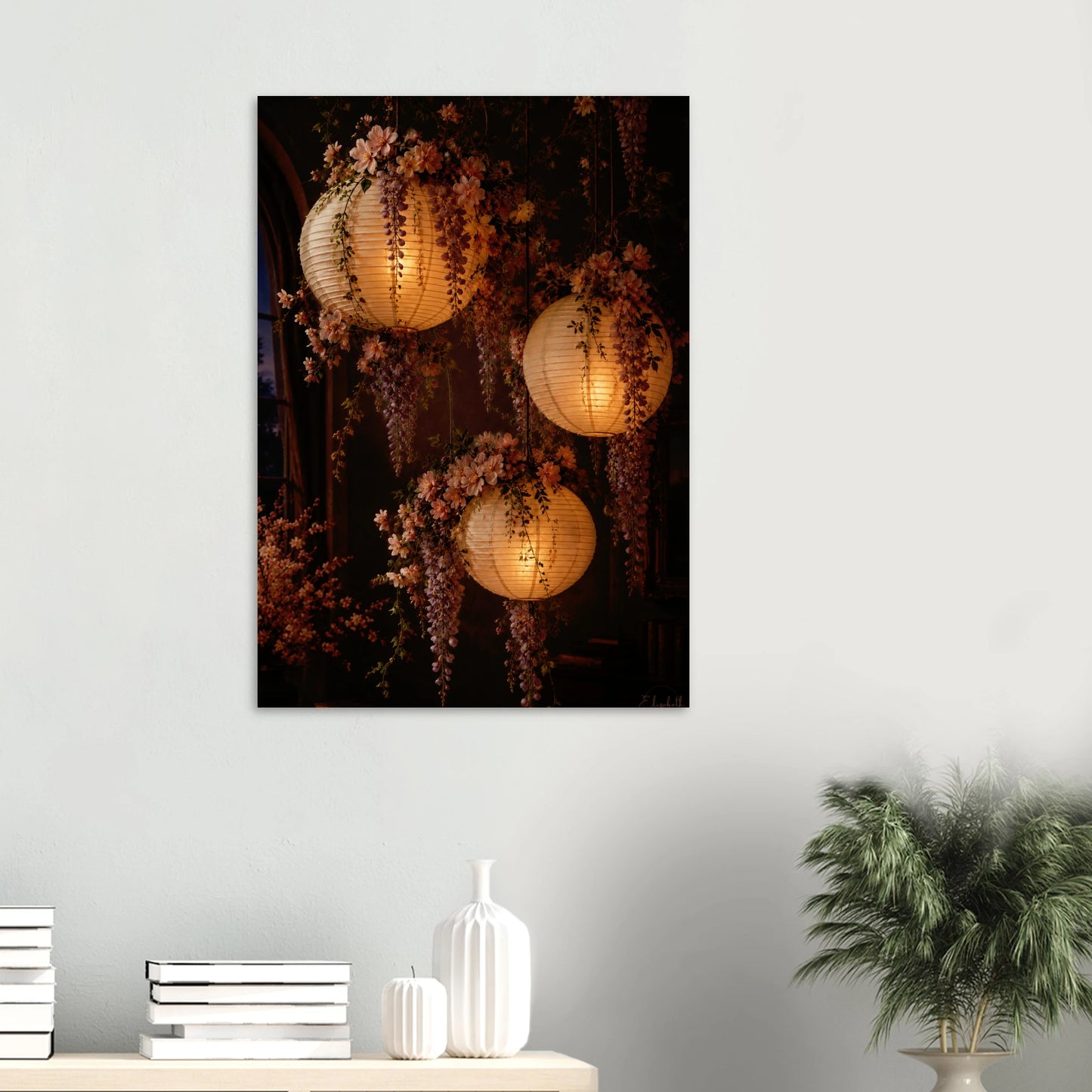 Three glowing paper lanterns hanging in a dim interior, decorated with cascading pink wisteria flowers and green leaves.