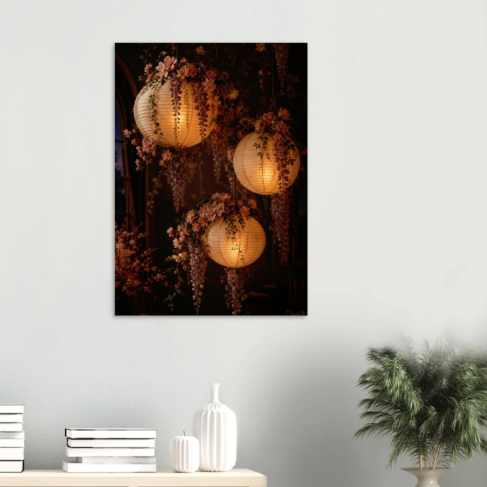 Three glowing paper lanterns hanging in a dim interior, decorated with cascading pink wisteria flowers and green leaves.