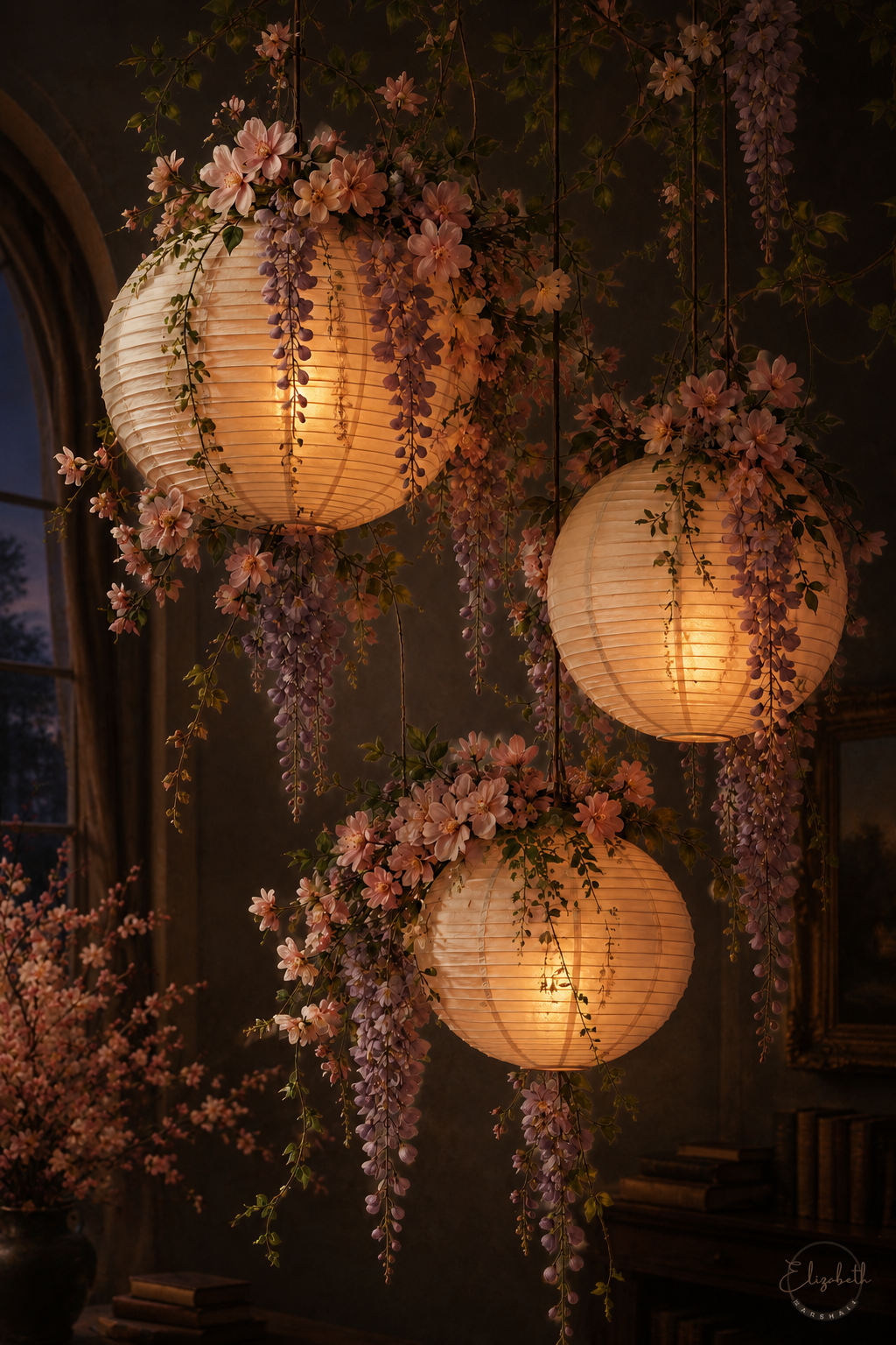 Three glowing paper lanterns hanging in a dim interior, decorated with cascading pink wisteria flowers and green leaves.