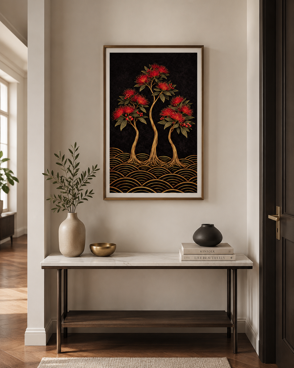A framed wall art print featuring three red-flowering trees with gold roots over a black background, displayed above a console table in a styled interior room.