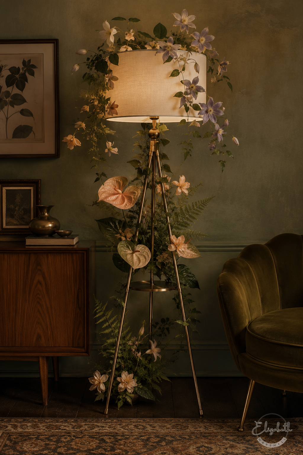 A vintage-style tripod floor lamp with a warm glowing cream shade, decorated with artificial green foliage, purple flowers, and pink tropical leaves, set in a cozy, dimly lit room next to a green velvet armchair.