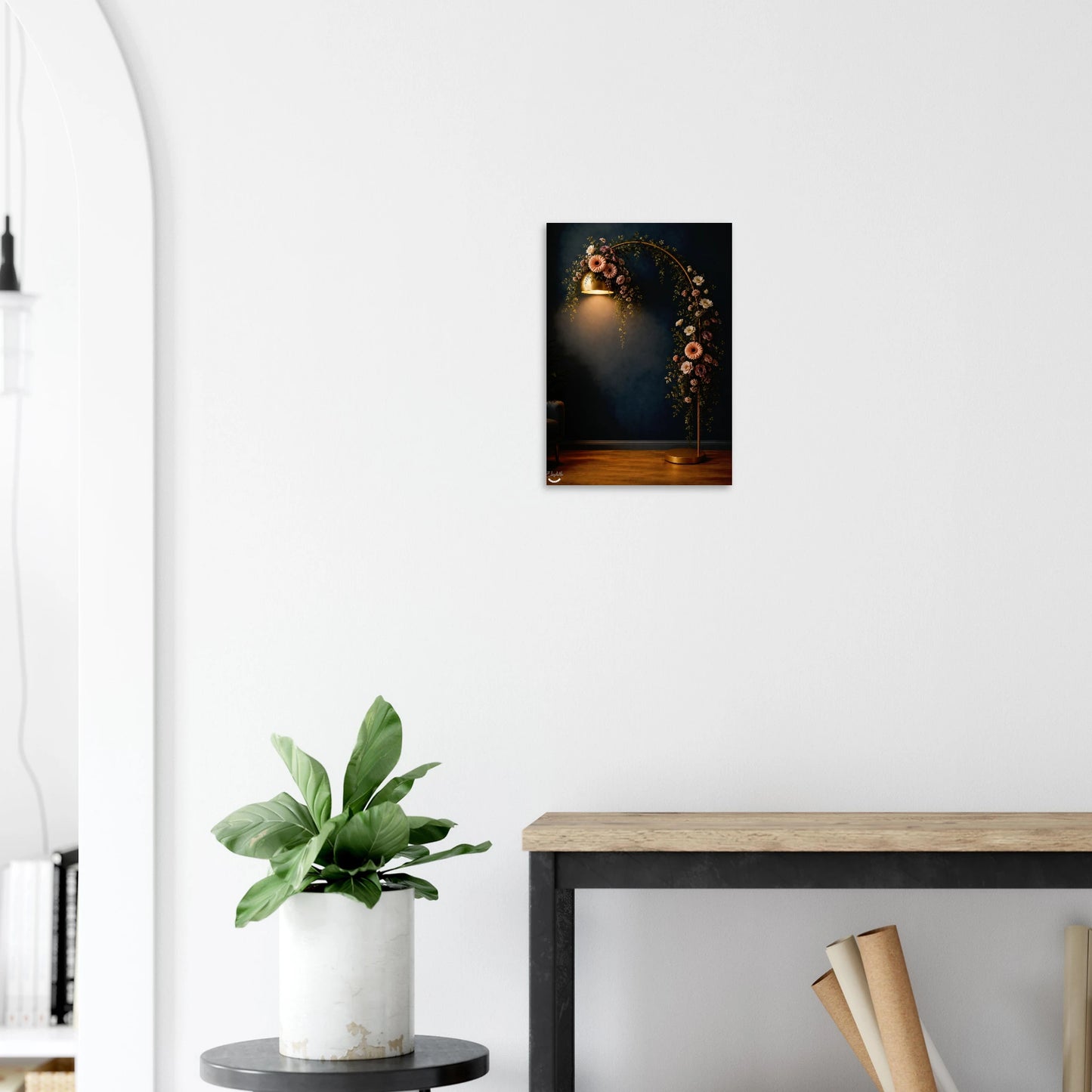 A small vertical wall art print showing a glowing floral arch against a dark background, displayed on a white wall above a console table with a potted plant nearby.