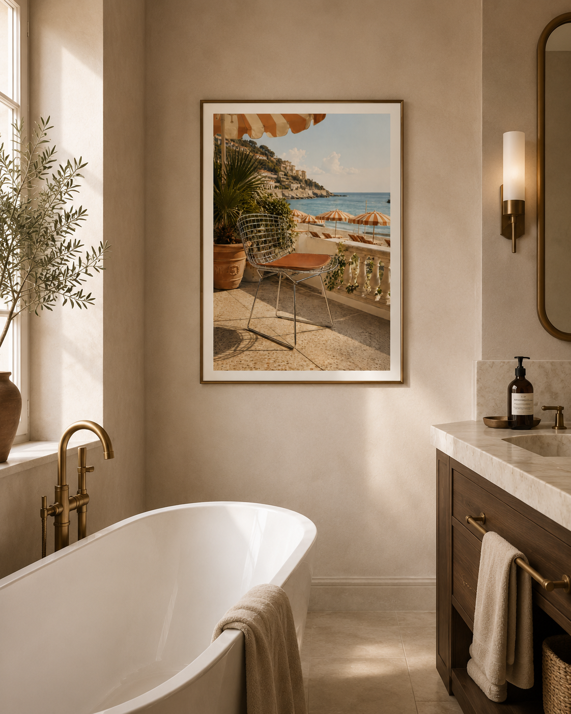A framed beach scene art print hangs on a beige wall in a modern bathroom with a white freestanding tub, brass fixtures, and a marble vanity.