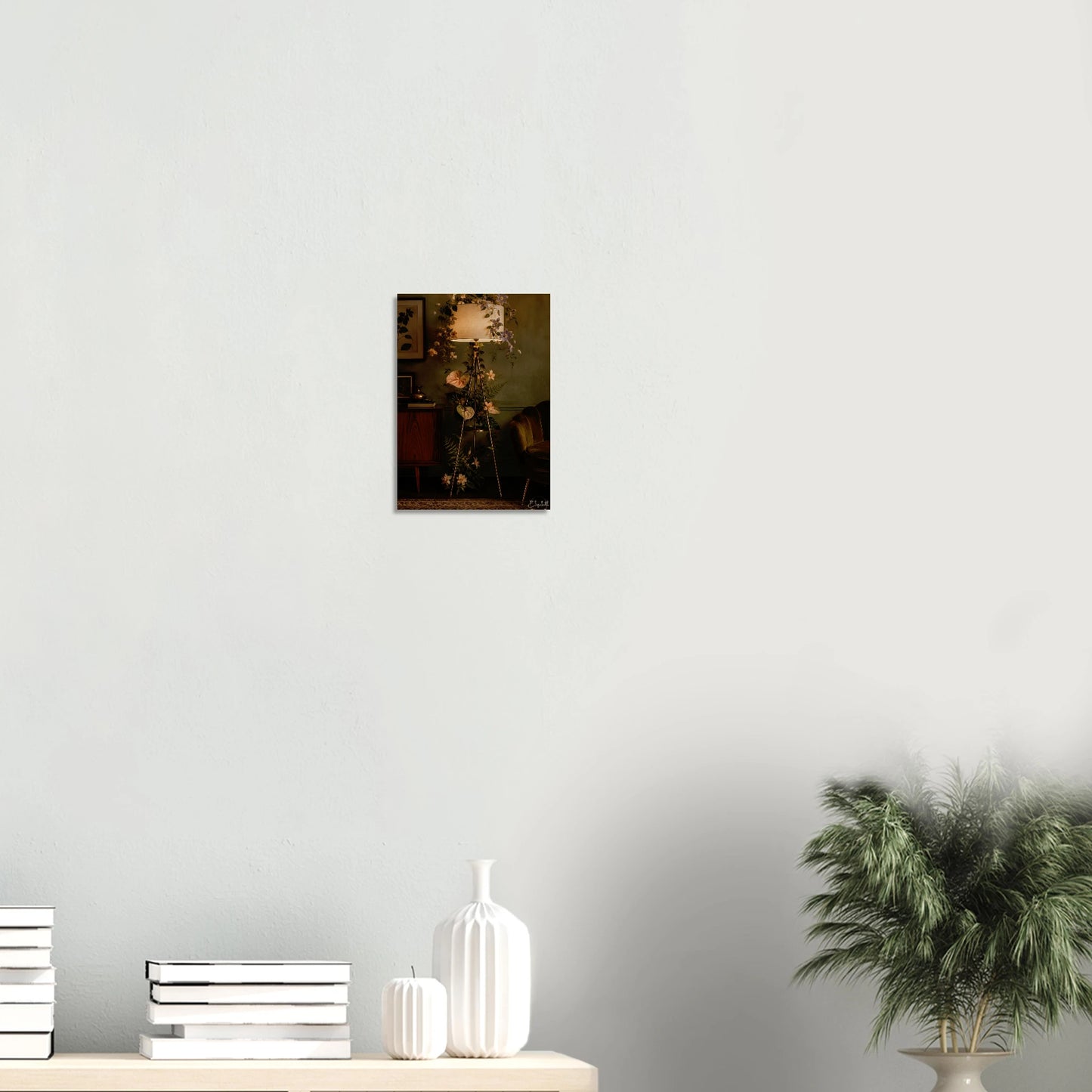 A small framed wall art print depicting a dark floral still life hangs on a light gray wall above a console table with stacked books, white vases, and a potted green plant.