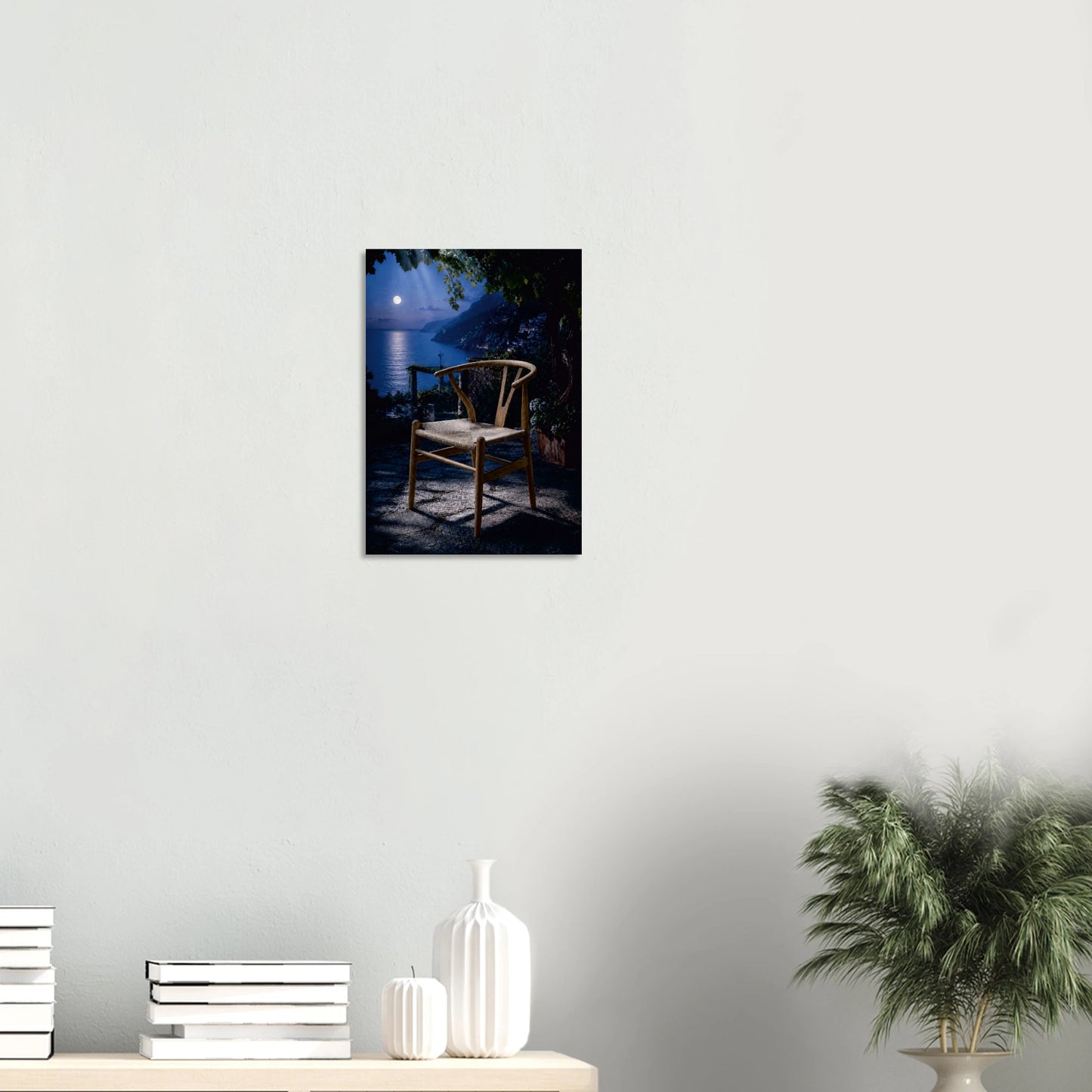 Wishing for a Moonlight Serenade is a love note to retro fans worldwide. A Wishbone Chair-inspired piece in warm natural wood sits alone on a moonlit terrace, the full moon hanging low over the water beyond, its reflection pooling across the deep midnight blue. Dark foliage presses in at the edges, a lantern glows softly to one side, and the whole scene holds its breath. It is the most romantic chair in the most romantic place, and it is waiting for someone to sit down and stay a while.