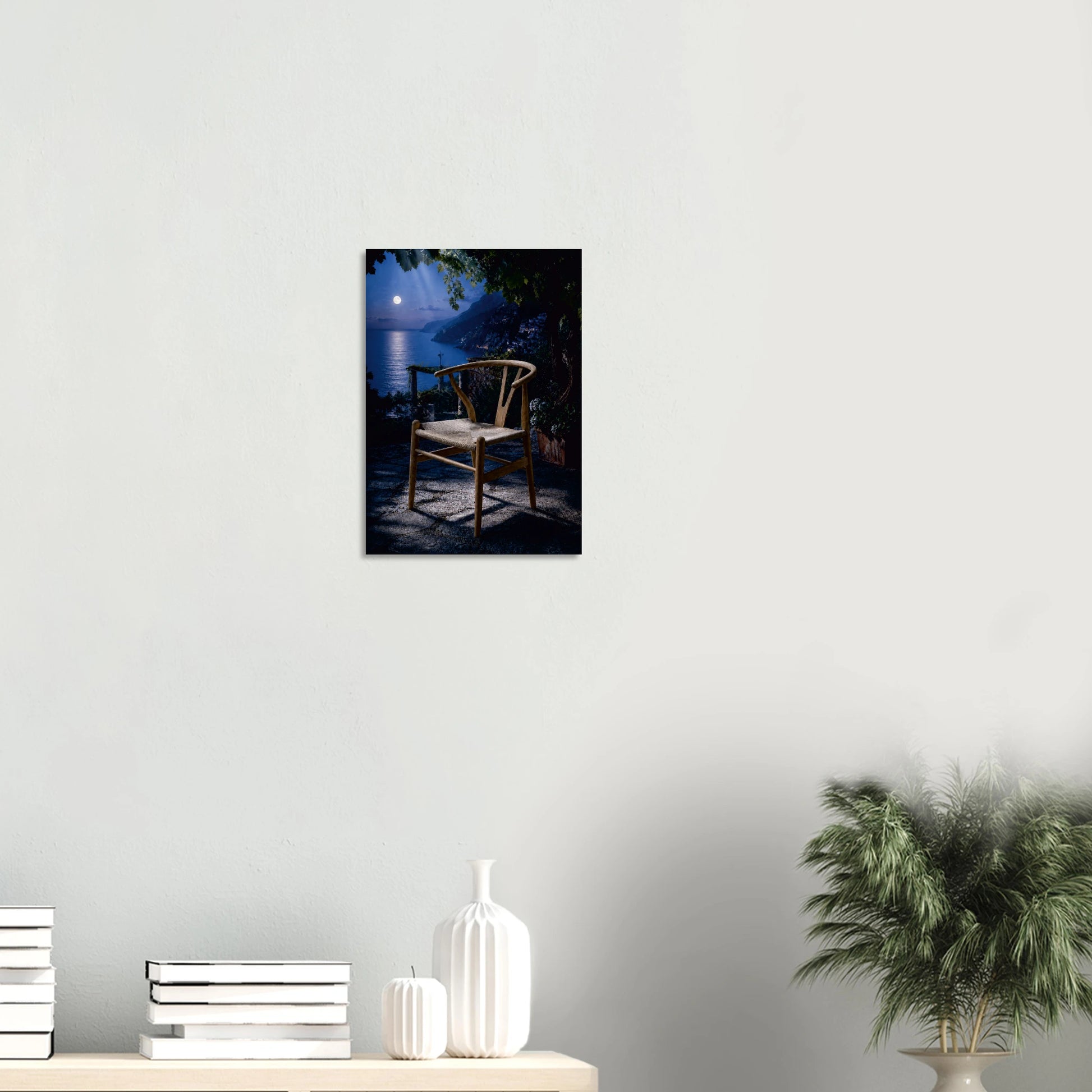 Wishing for a Moonlight Serenade is a love note to retro fans worldwide. A Wishbone Chair-inspired piece in warm natural wood sits alone on a moonlit terrace, the full moon hanging low over the water beyond, its reflection pooling across the deep midnight blue. Dark foliage presses in at the edges, a lantern glows softly to one side, and the whole scene holds its breath. It is the most romantic chair in the most romantic place, and it is waiting for someone to sit down and stay a while.