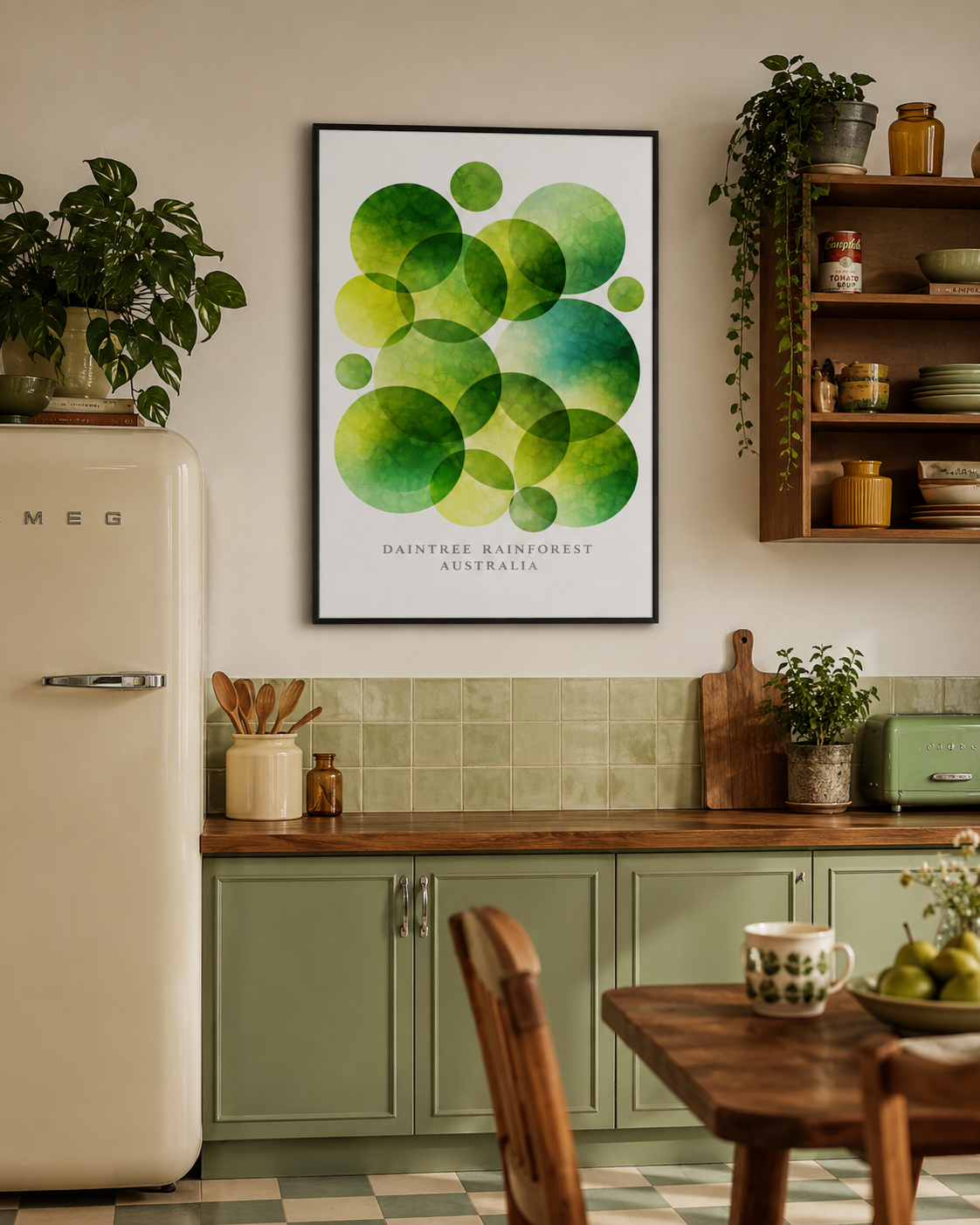 A framed art print featuring green watercolor circles with the text 'DAINTHIE RAINFOREST AUSTRALIA' hanging on a kitchen wall above sage green cabinets and a wooden table.