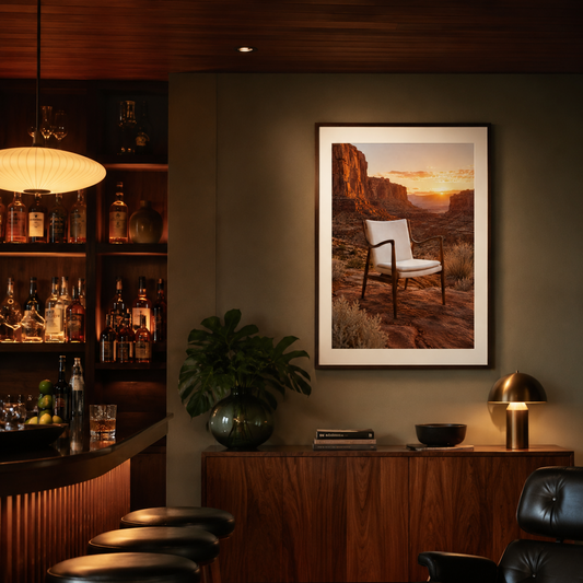 The Chair Chased the Sunset and made it all the way to the canyon. A Finn Juhl 45 Chair-inspired piece, its sculpted dark wooden frame and cream upholstered seat perfectly composed, sits alone in a vast red canyon landscape as the sun burns low between the mesa walls. Everything is amber and terracotta and the particular kind of quiet that only exists at golden hour in a place this big. The chair looks completely at ease. It has been here before.