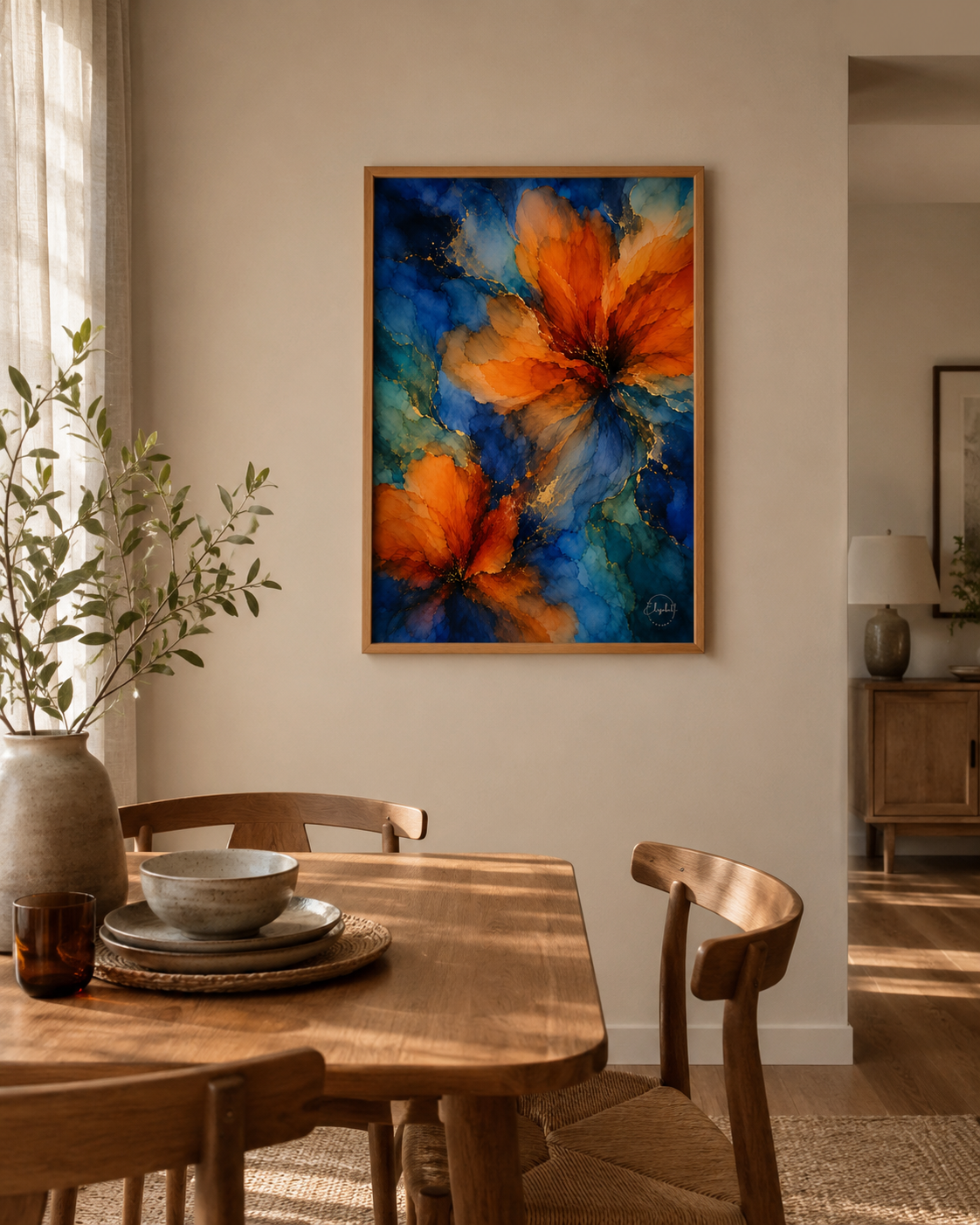 A framed abstract floral painting with vibrant orange and blue flowers hangs on a beige wall above a wooden dining table in a warm, modern dining room.