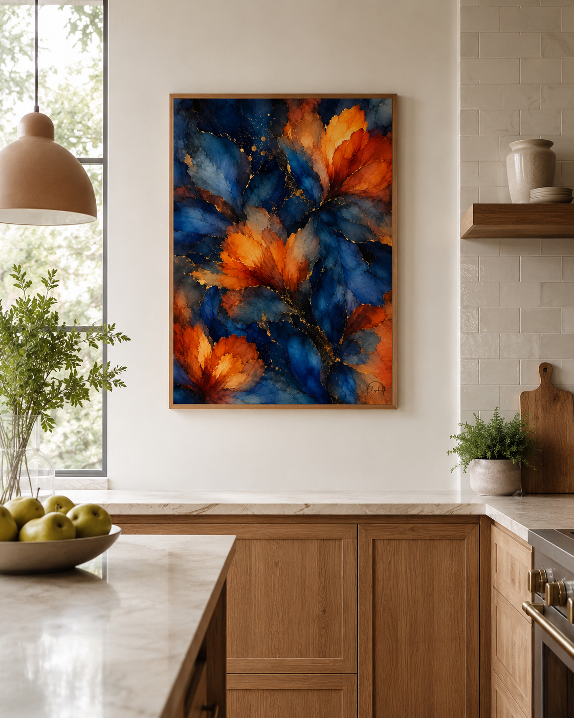 A framed abstract floral painting with vibrant blue and orange leaves hangs on a white kitchen wall above a wooden countertop.