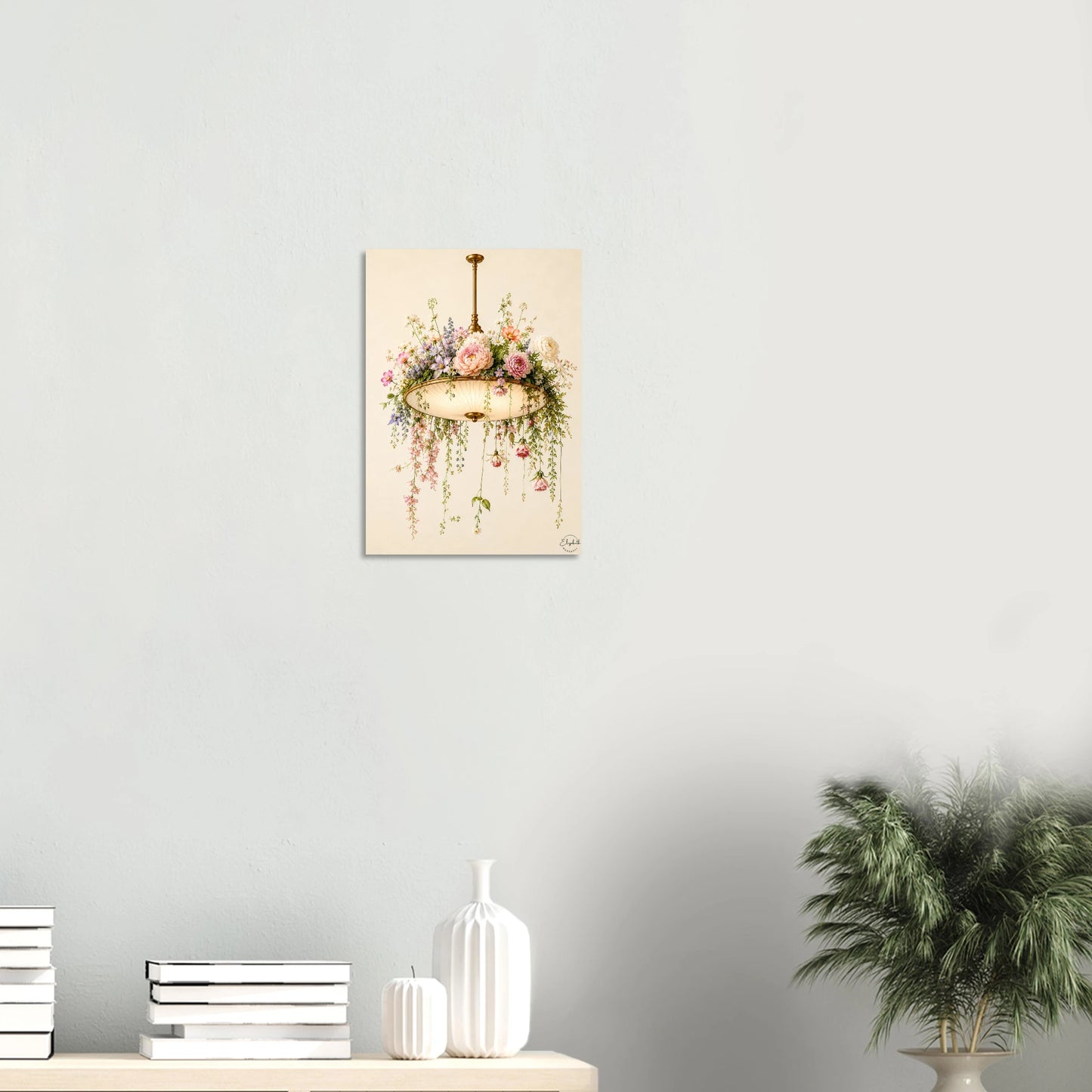 A vertical art print depicting a vintage gold chandelier adorned with pink and white flowers and green foliage, hanging on a light gray wall above a styled shelf with books, vases, and a potted plant.
