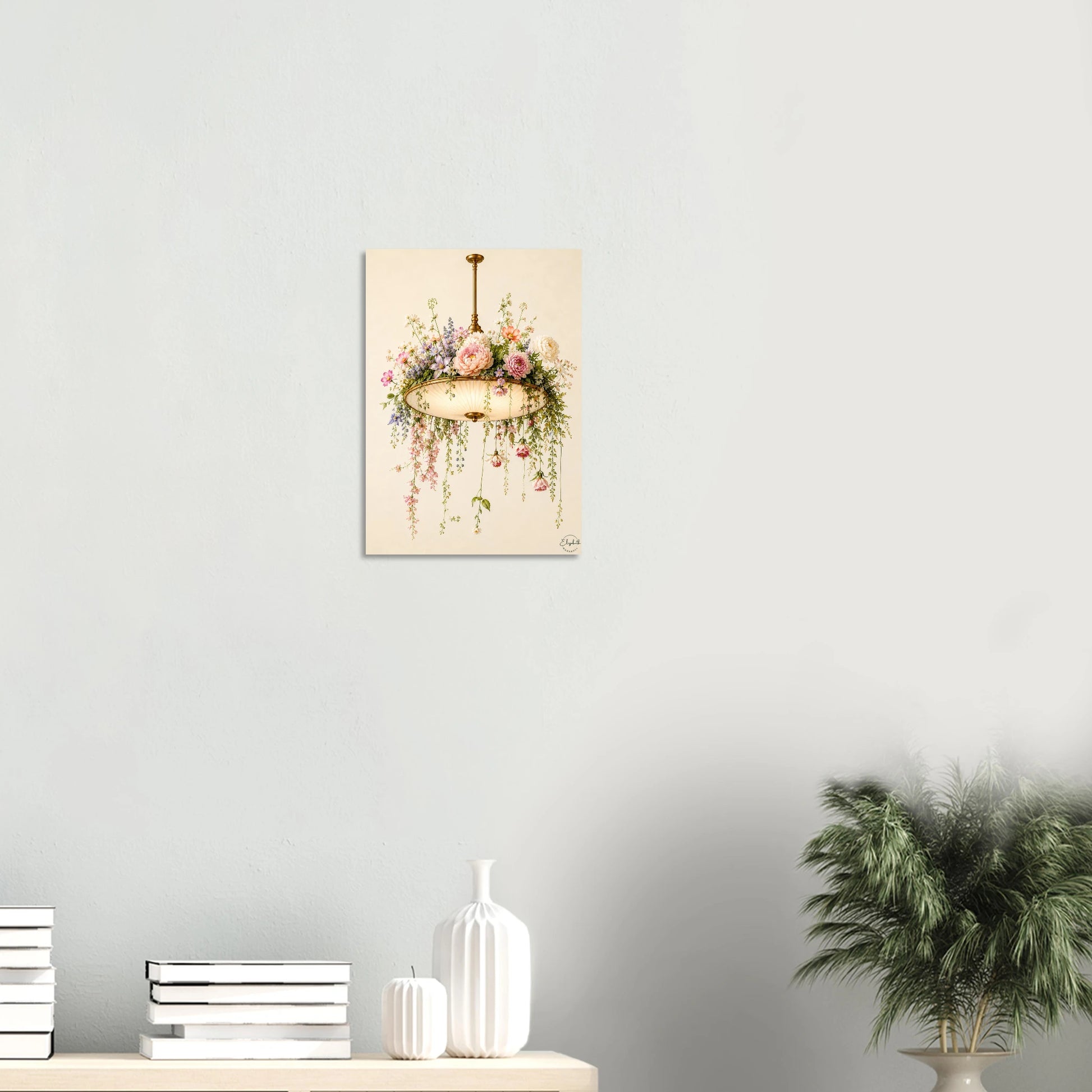 A vertical art print depicting a vintage gold chandelier adorned with pink and white flowers and green foliage, hanging on a light gray wall above a styled shelf with books, vases, and a potted plant.