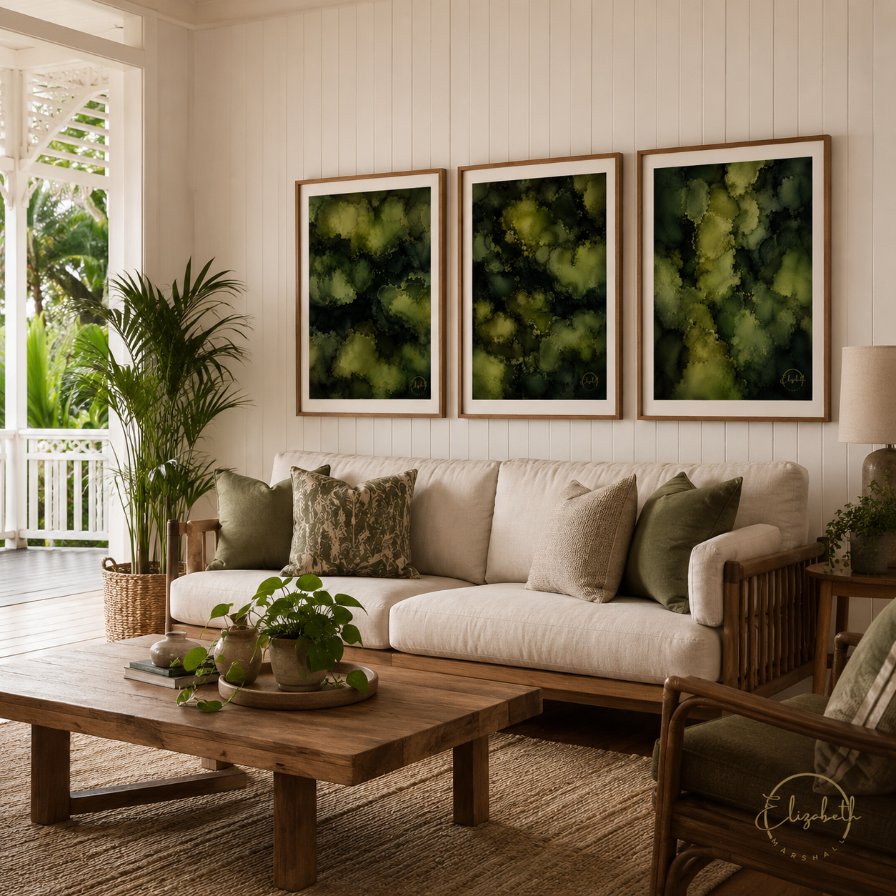 Three framed abstract green and black art prints hang above a beige sofa in a bright, tropical-style living room with a wooden coffee table, potted plants, and a window view.