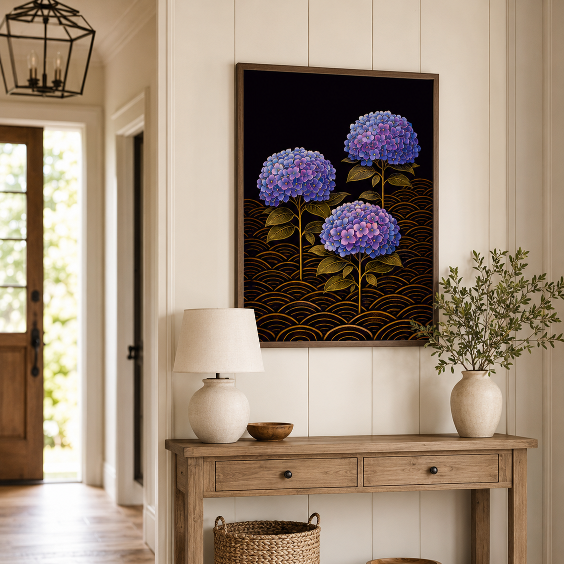 A framed vertical canvas print of three purple-blue hydrangeas on a dark background with gold wave patterns, hanging on a cream paneled wall above a rustic wooden console table in a bright hallway.