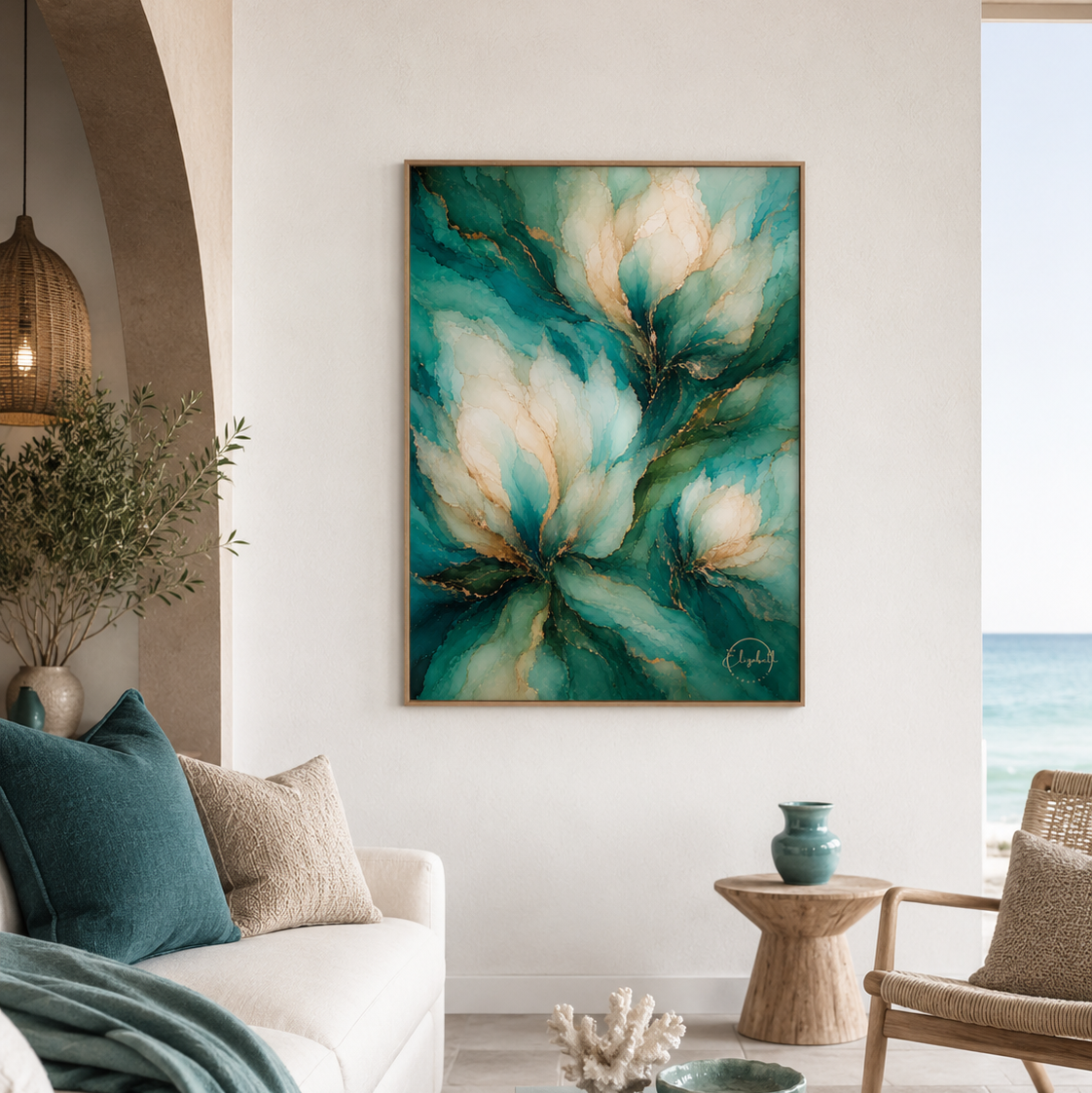 A framed abstract floral painting in teal, cream, and gold hangs on a white wall in a modern, sunlit living room with a sofa, side table, and ocean view.