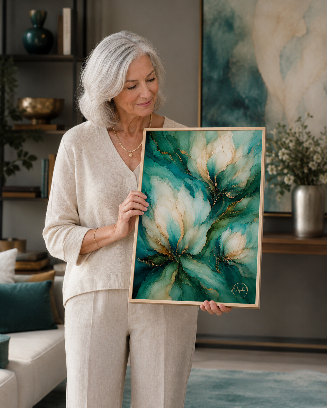 An older woman with silver hair stands in a living room holding a framed abstract painting. The artwork features swirling teal, green, cream, and gold tones.