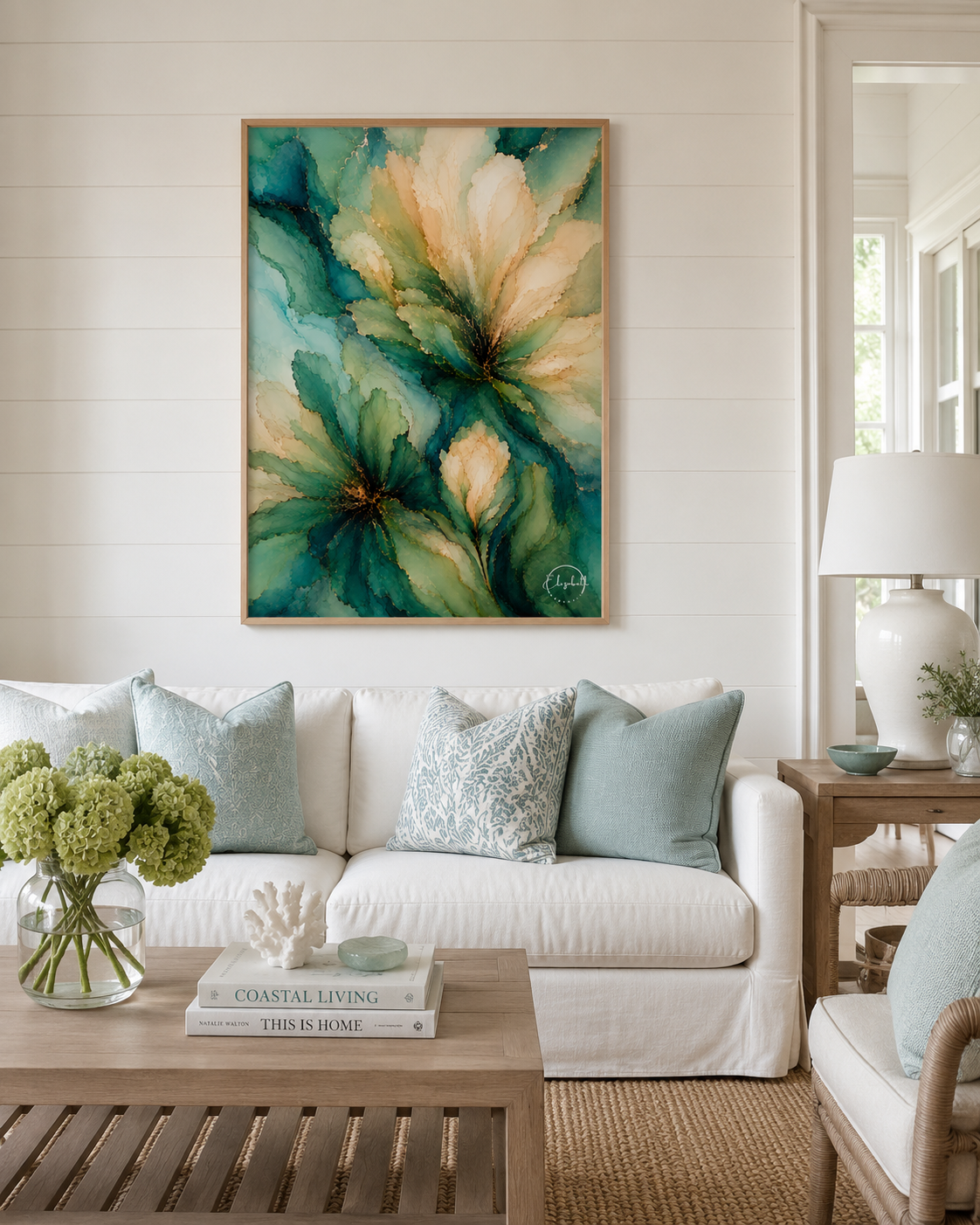 A framed abstract floral painting in teal, green, and cream tones hangs on a white shiplap wall above a white sofa with light blue pillows in a bright, modern living room.