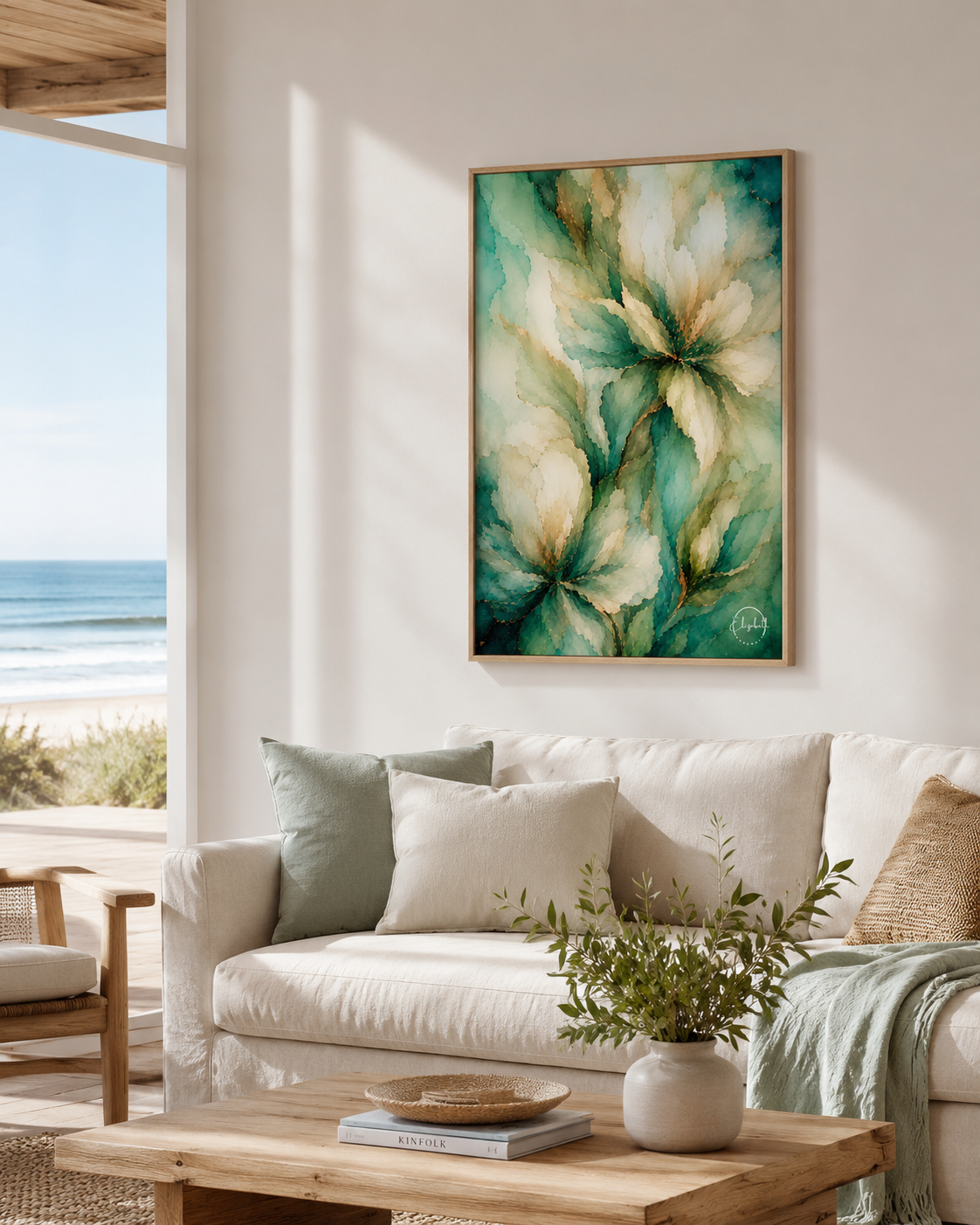 A framed abstract floral painting in teal, green, cream, and gold tones hangs on a white wall above a beige sofa in a bright living room with a window overlooking the ocean.