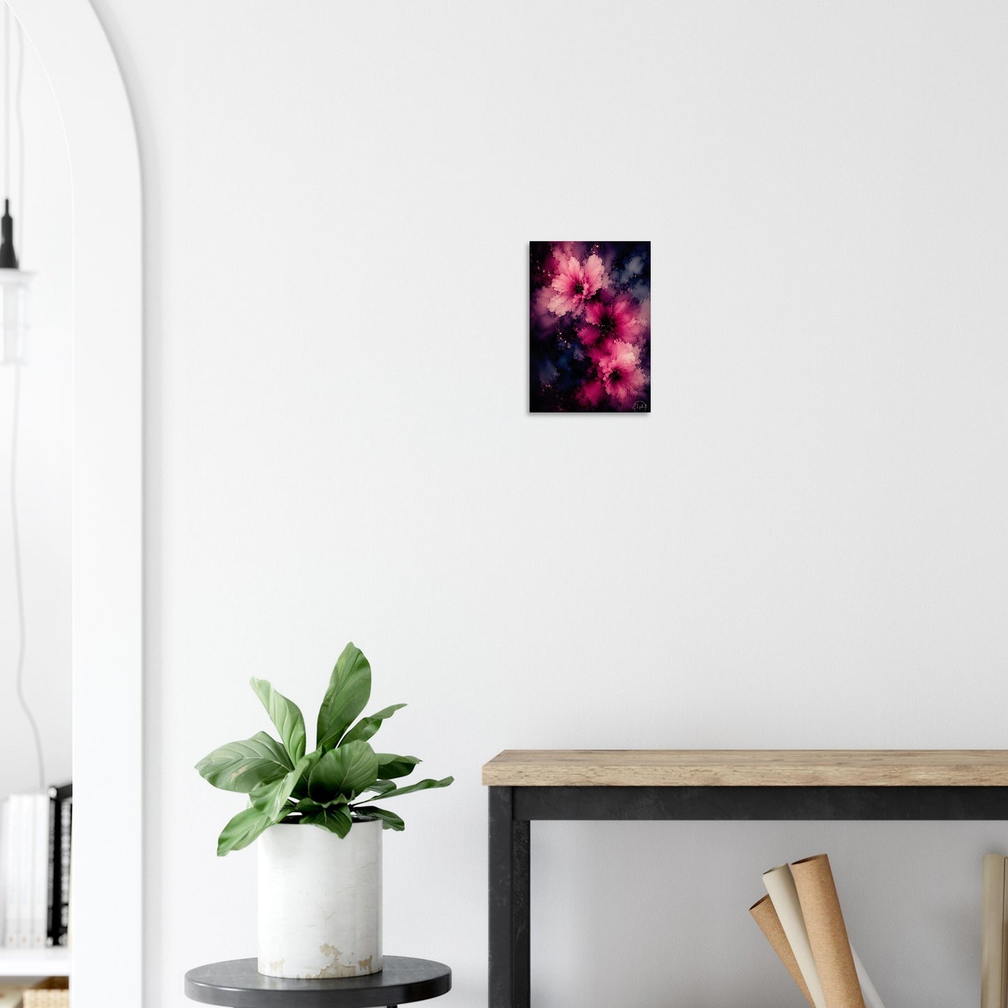 A small vertical wall art print featuring pink and magenta flowers against a dark background, displayed on a white wall above a wooden console table with a potted green plant in a modern interior setting.
