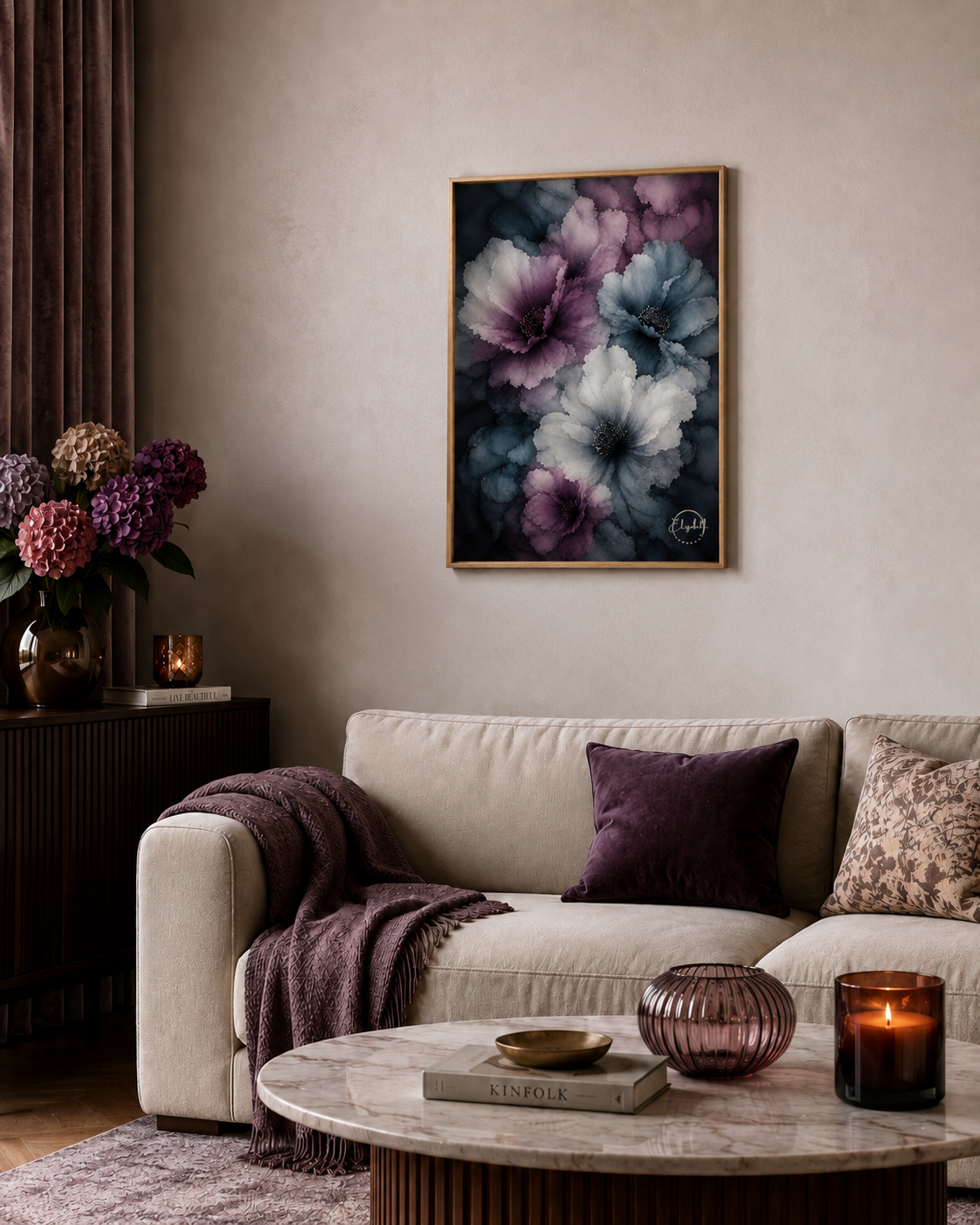 A framed floral wall art print with large purple, blue, and white flowers hangs above a beige sofa in a styled living room with a round marble coffee table, cushions, and candles.