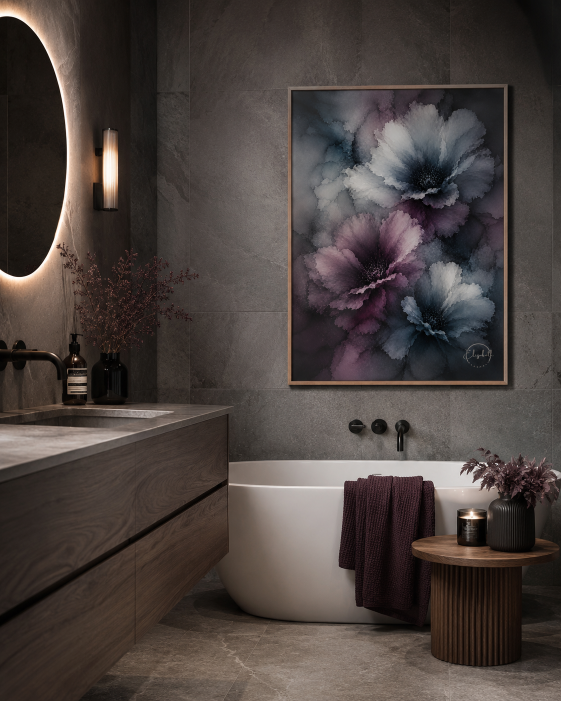 A framed wall art print featuring large abstract flowers in blue, purple, and gray tones, displayed above a white freestanding bathtub in a modern bathroom with a wood vanity, round wall mirror, and small side table.