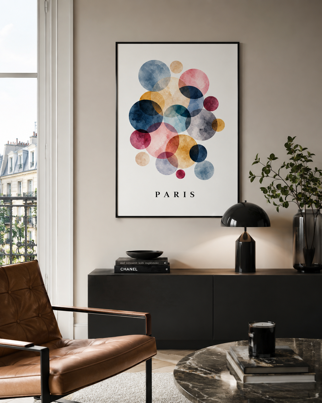 A framed wall art print featuring overlapping watercolor circles in blue, pink, yellow, and purple on a white background with the word PARIS below, displayed in a modern living room setting.