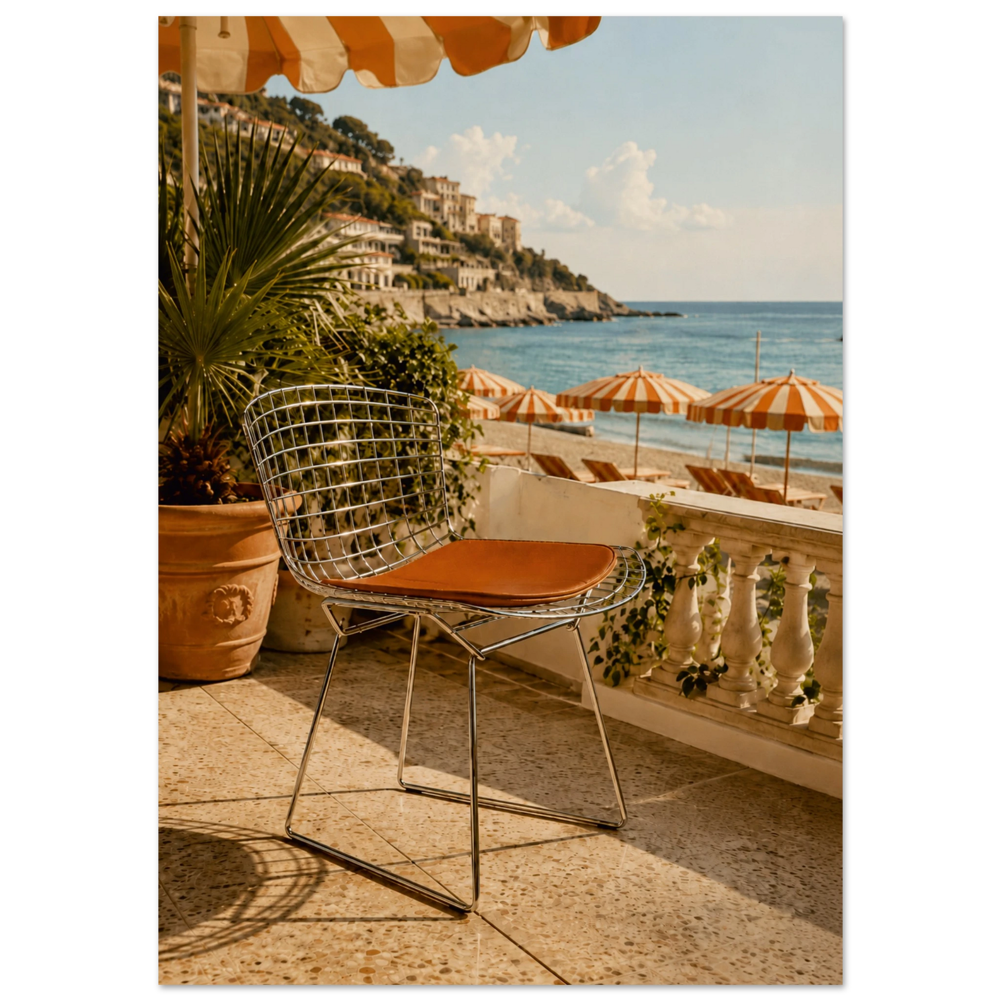 A modern wire chair with a brown cushioned seat sits on a sunlit terrace overlooking a coastal beach with blue water, lounge chairs, and striped umbrellas.