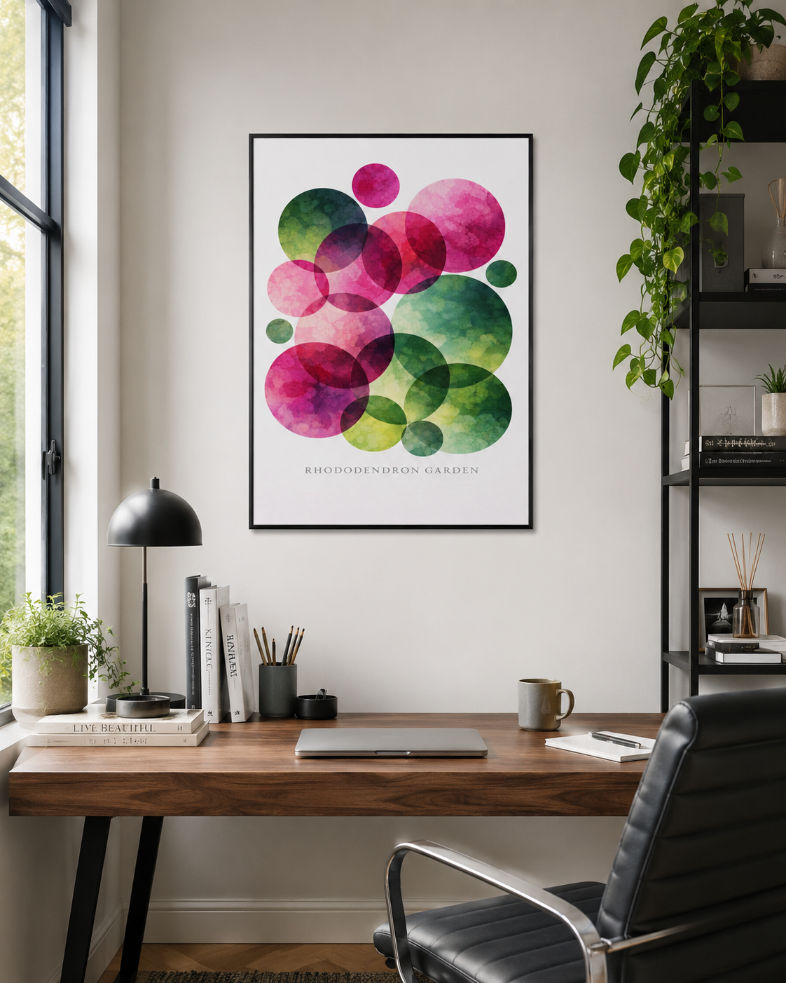A framed abstract art print featuring overlapping colorful circles in pink, green, and purple, displayed on a light gray wall above a wooden desk in a modern home office setting.