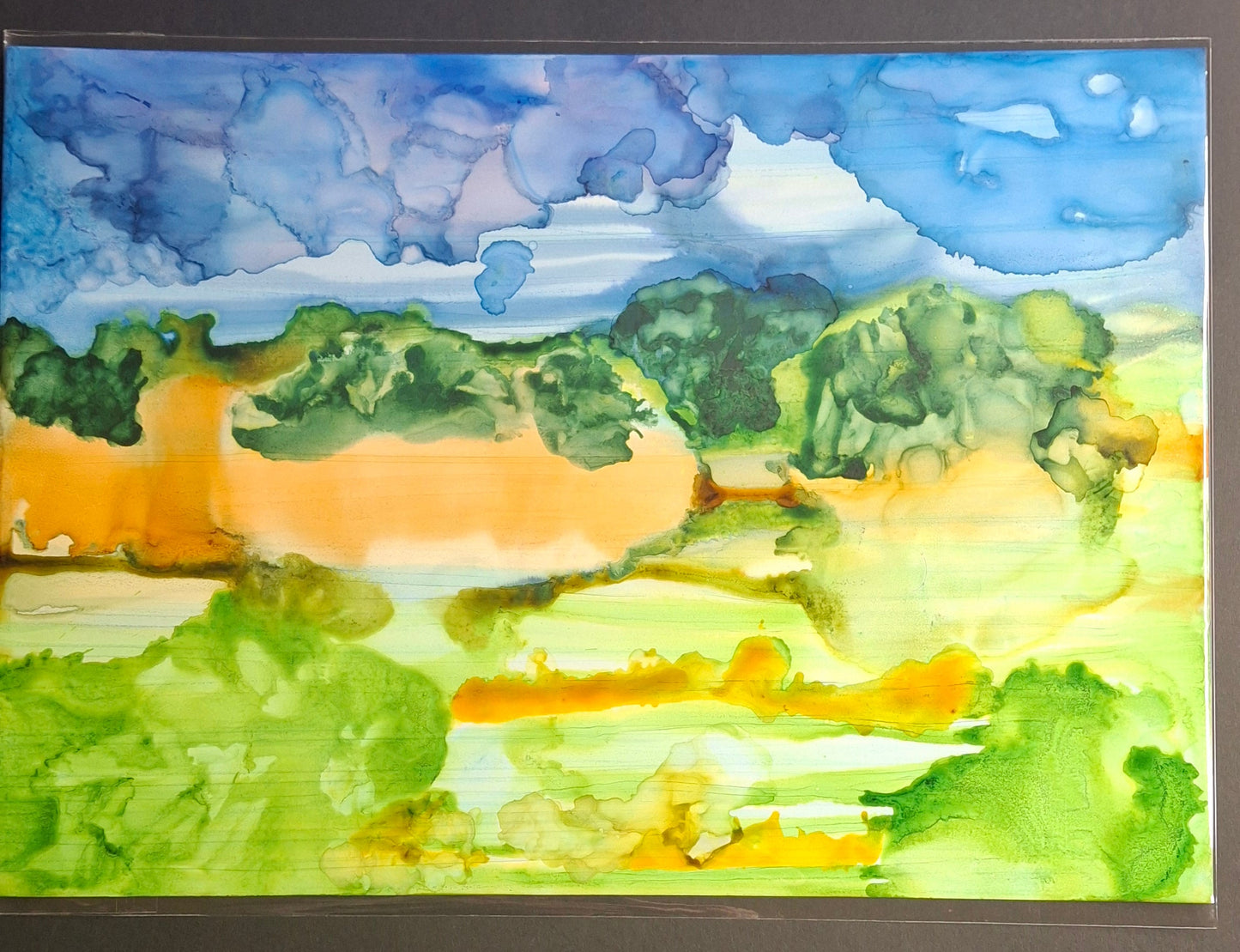 A horizontal watercolor landscape painting featuring green fields, orange hills, and a blue sky, displayed against a dark gray background.