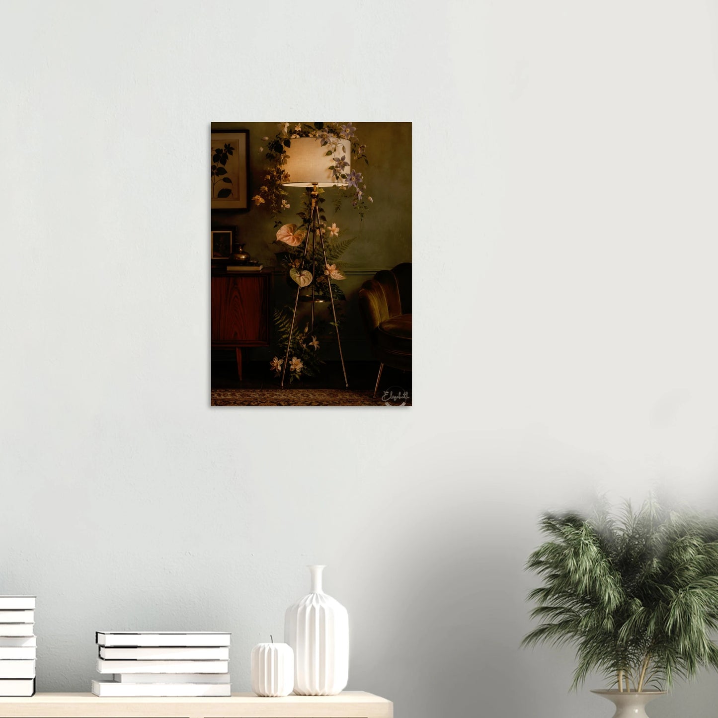 A vertical framed wall art print depicting a moody vintage interior with a glowing floor lamp, flowers, and dark furniture, displayed on a light gray wall above a console table with books and white vases.