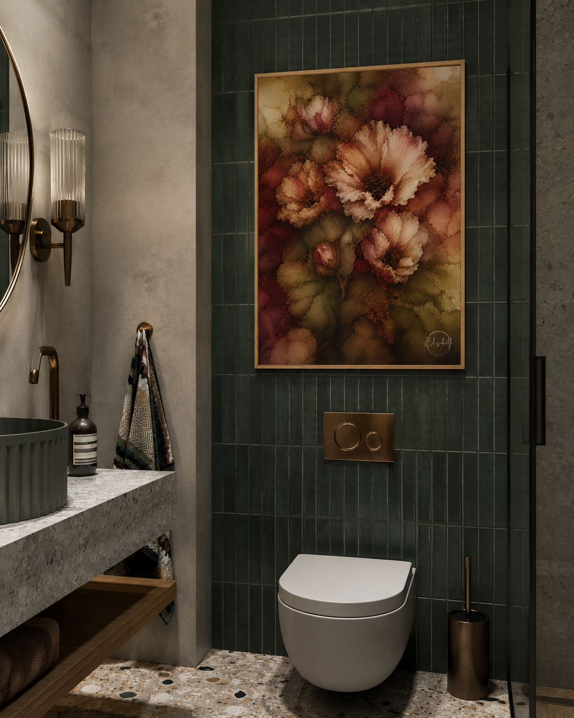 A framed floral wall art print with muted pink, brown, and green tones hangs on a dark green tiled bathroom wall above a white wall-mounted toilet. The bathroom also includes a stone countertop, round mirror, wall sconces, and a brass flush plate.