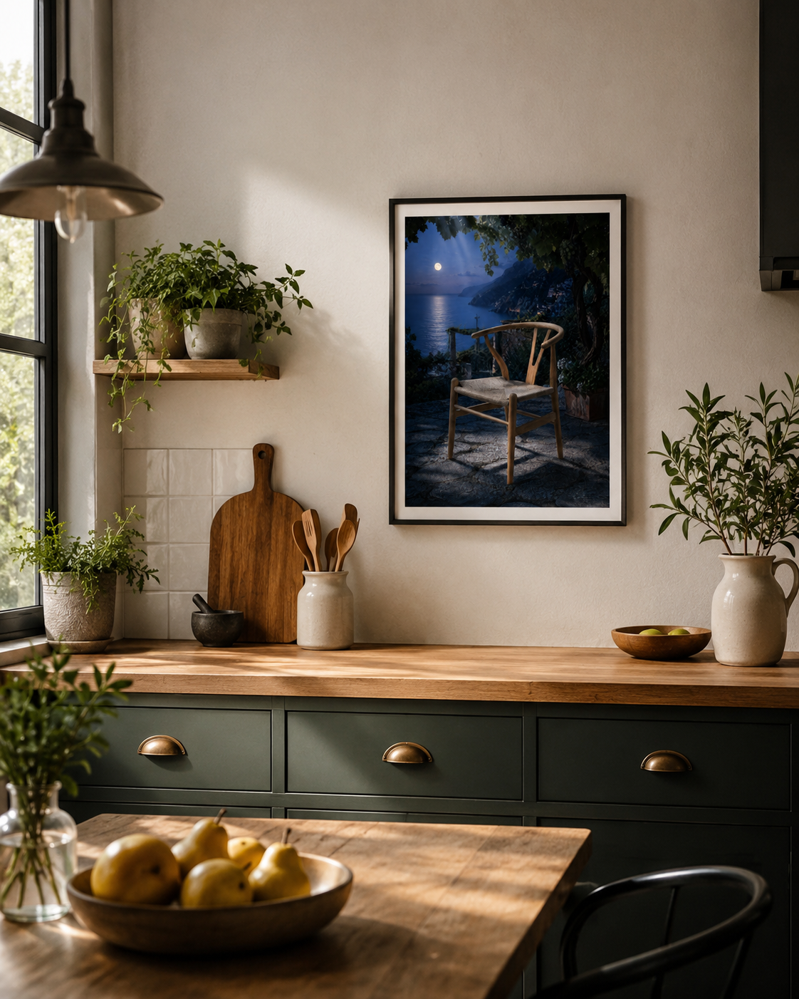 A framed art print depicting a moonlit night scene with a wooden chair and water, displayed on a beige wall in a styled kitchen setting with green cabinets, wooden countertops, and potted plants.